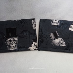 May include: Two gray fabric wallet-sized pouches with a black and white skull and top hat pattern. The pattern includes spiders and spiderwebs.
