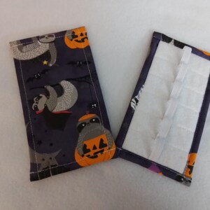 May include: Two fabric pouches, one with a Halloween-themed print of sloths and pumpkins on a dark purple background, and the other with a white, padded interior and a dark purple exterior.