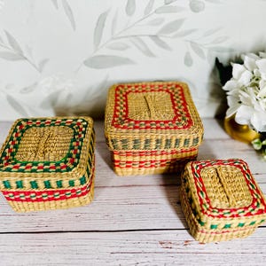 May include: Three woven storage boxes with red, green, and natural colored trim. The boxes are made of natural materials and have a rustic look.