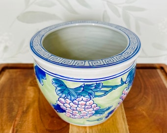 May include: A white ceramic planter with a blue and green grape design. The planter has a blue and white geometric border around the top.