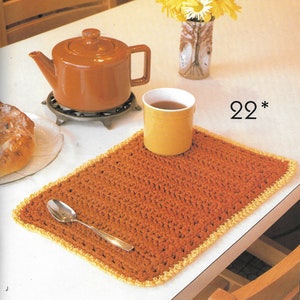 May include: A brown crocheted placemat with a yellow border, a yellow mug, a spoon, and a plate with a pastry on a white table. The text "22*" is visible in the image.
