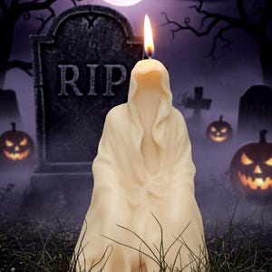 Può includere: Una candela color crema a forma di figura incappucciata, con una fiamma accesa. La candela è ambientata su uno sfondo di Halloween con una lapide con la scritta "RIP", zucche intagliate e una luna piena in un cielo viola.