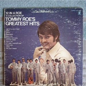 Könnte beinhalten: Ein Vintage-Vinyl-Plattencover mit einem Foto von Tommy Roe, einem Singer-Songwriter, mit dem Titel "12 In A Roe: A Collection of Tommy Roe's Greatest Hits". Das Albumcover ist blau und zeigt ein Foto von Tommy Roe in einem weißen Hemd, mit einer Gruppe von Musikern hinter ihm.