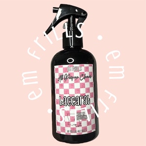 以下が含まれることがあります： ピンクと白のチェック柄のラベルが付いた黒いプラスチック製のスプレーボトル。ラベルには「EM FRILLS」、「All Purpose Cleaner」、「baccarat」、「MADE IN LOUISIANA」の文字と州の輪郭が描かれています。容量は236mlです。