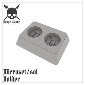 May include: A gray plastic Microset/sol holder with two circular indentations, each featuring a skull design. The holder has a rectangular shape and the text "Rouge Plastic" and "Microset/sol Holder" are visible.