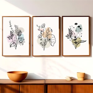 May include: Three framed prints with black line drawings of floral bouquets on a white background. Each print has a different arrangement of flowers and leaves with abstract pastel colored shapes behind them.