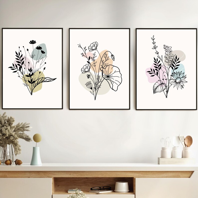 May include: Set of three black and white line art prints featuring floral bouquets with abstract shapes in pastel colors. The prints are framed in black frames and hung on a white wall.