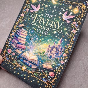 Könnte beinhalten: Ein rechteckiges Notizbuch mit Fantasy-Motiv. Der Einband zeigt den Text "THE FANTASY BOOK CLUB". Illustrationen umfassen ein Schloss, Bücher, Vögel, Sterne und florale Akzente, alles vor einem dunkelblauen Hintergrund.