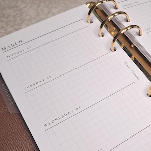 Può includere: Un'agenda in pelle marrone aperta su una pagina settimanale di marzo 2024. Le pagine sono bianche con un motivo a griglia e anelli color oro. L'agenda è aperta per la settimana dal 2 all'8 marzo, con il logo "Elmia Designs" visibile.