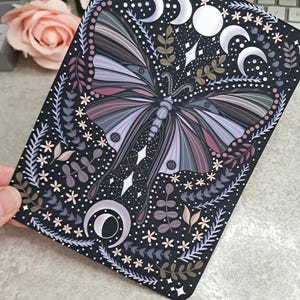 May include: A black background with a large, detailed, purple and grey butterfly with a silver glitter effect. The butterfly is surrounded by small white flowers, green leaves, and silver crescent moons.