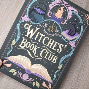 Może przedstawiać: Ciemnozielona okładka książki z napisem "Witches' Book Club" w kremowym skrypcie. Okładka zawiera ilustracje kotła, płomienia, czarnego kota i otwartej książki z fioletowymi stronami, wszystko w dekoracyjnej ramie.