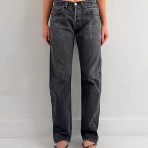 May include: High-waisted charcoal grey denim jeans featuring a straight-leg cut, a classic five-pocket design, a button fly closure with a silver-toned metal button, and copper-coloured rivets at the pocket corners, finished with a standard hem.