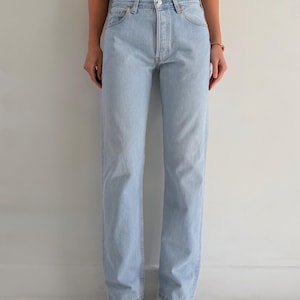 Può includere: Jeans in denim azzurro con vita alta, design classico a cinque tasche, chiusura con bottoni e gamba dritta. Il denim presenta un lavaggio chiaro con cuciture visibili lungo le gambe, le tasche e la fascia in vita.