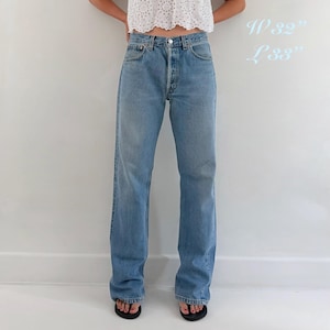 May include: Light blue denim jeans with a classic five-pocket design, a button fly, and a straight-leg cut. The jeans feature a medium wash and are labeled with the measurements W 32" L 33" printed in light blue text on the right side of the image.
