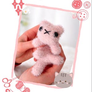 May include: A small, pink, crocheted cat with black eyes and a stitched mouth. The cat is held in a person's hands. The image includes the text "Itty Bitty Pocket Kitty" and "Crochet Pattern".