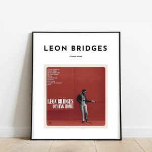 May include: A black and white framed poster with the title "LEON BRIDGES COMING HOME" in white text. The poster features a red background with a black and white photo of a man in a leather jacket standing in front of a red wall. The album cover lists the songs "Coming Home", "Better Man", "River", "Treadin' & Groovin'" and more.