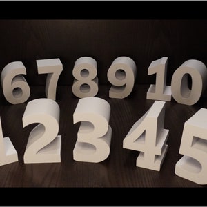 May include: White foam numbers from one to ten, arranged in a semi-circle on a dark wood surface. The numbers are three-dimensional and have a hollow centre.