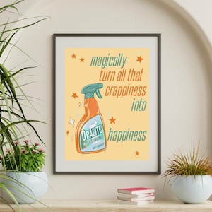 Può includere: Stampa incorniciata con sfondo giallo chiaro. Presenta un'illustrazione di un flacone spray arancione con il testo "trasforma magicamente tutta quella schifezza in felicità". Il flacone spray è etichettato "Opalite Magical Results".