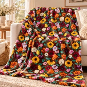 Puede incluir: Una manta de felpa con fondo marrón oscuro y un vibrante patrón floral repetitivo. El diseño incluye girasoles amarillos, flores de color rojo intenso, naranja y pétalos de color violeta claro, unidos por tallos y hojas de color verde.