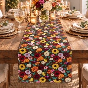 May include: A rectangular table runner featuring a dark brown background with a dense, colorful floral pattern of yellow sunflowers, red poppies, orange blossoms, and white flowers with green leaves, laid flat on a wooden dining table.