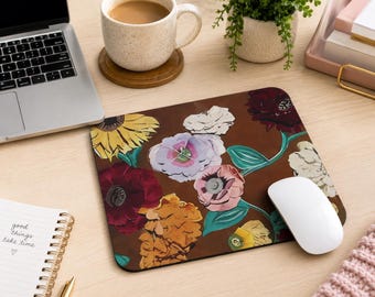 May include: A rectangular mouse pad featuring a dark brown background with a vibrant floral pattern. The design includes illustrations of a yellow sunflower, deep red roses, a pale purple flower, and a soft pink bloom with green leaves.