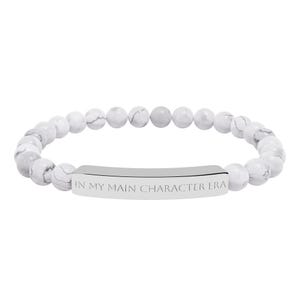 Peut inclure: Bracelet compos&eacute; de perles blanches et grises, avec une barre argent&eacute;e grav&eacute;e de l'inscription "IN MY MAIN CHARACTER ERA". Les perles rondes ont un aspect marbr&eacute;.