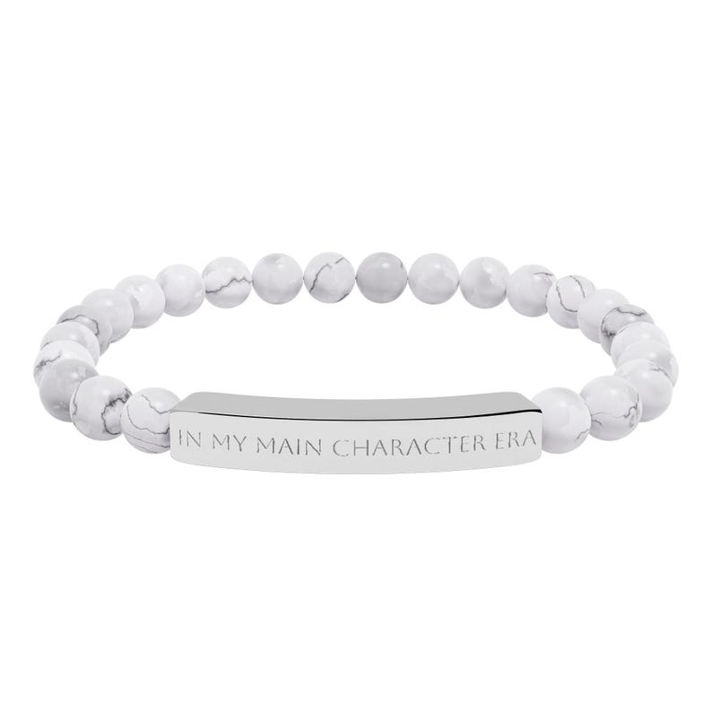 Peut inclure: Bracelet compos&eacute; de perles blanches et grises, avec une barre argent&eacute;e grav&eacute;e de l'inscription "IN MY MAIN CHARACTER ERA". Les perles rondes ont un aspect marbr&eacute;.