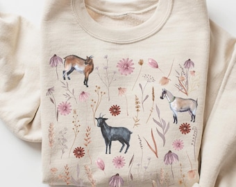 May include: A beige sweatshirt with a watercolor design of goats and flowers. The goats are brown, black, and white. The flowers are pink and purple.
