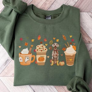 May include: Military green sweatshirt with a fall-themed graphic. The design features coffee cups, autumn leaves, and a dog wearing a scarf and boots. The text "MILITARY GREEN" is at the bottom.
