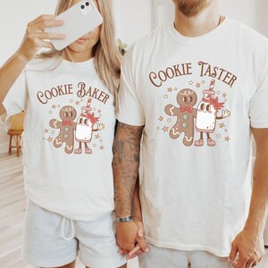 May include: Two white t-shirts with a gingerbread man and milk carton design. The text on the shirts reads "Cookie Baker" and "Cookie Taster".
