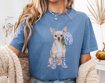 May include: A blue jean t-shirt with a graphic of a chihuahua wearing blue and white rain boots and holding a bouquet of blue hydrangeas.