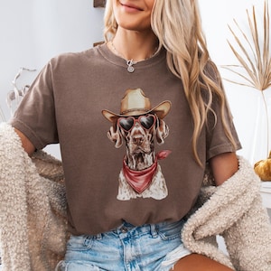 May include: A brown t-shirt with a graphic of a dog wearing a cowboy hat and heart-shaped sunglasses. The dog is wearing a red bandana around its neck. The text "ESPRESSO" is visible at the bottom of the image.