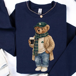 May include: Navy blue sweatshirt featuring a cartoon bear dressed in a tan coat, green scarf, and a hat with a shamrock. The bear is holding a glass of dark beer. The word "NAVY" is printed at the bottom of the sweatshirt.