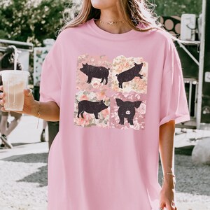 May include: A pink oversized t-shirt with a graphic print of four black pigs in a floral pattern.