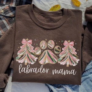 May include: Brown sweatshirt with a Christmas tree and paw print design. The text "labrador mama" is printed on the front.