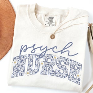 May include: A cream colored t-shirt with the text "psych NURSE" in blue with a floral pattern. The word "NURSE" is in a large, bold font.