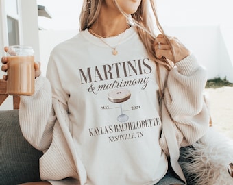 May include: White sweatshirt with the text "MARTINI'S & matrimony" and a martini glass graphic. The text "MAY 2024" is above the glass and the text "KAYLA'S BACHELORETTE NASHVILLE, TN" is below the glass.