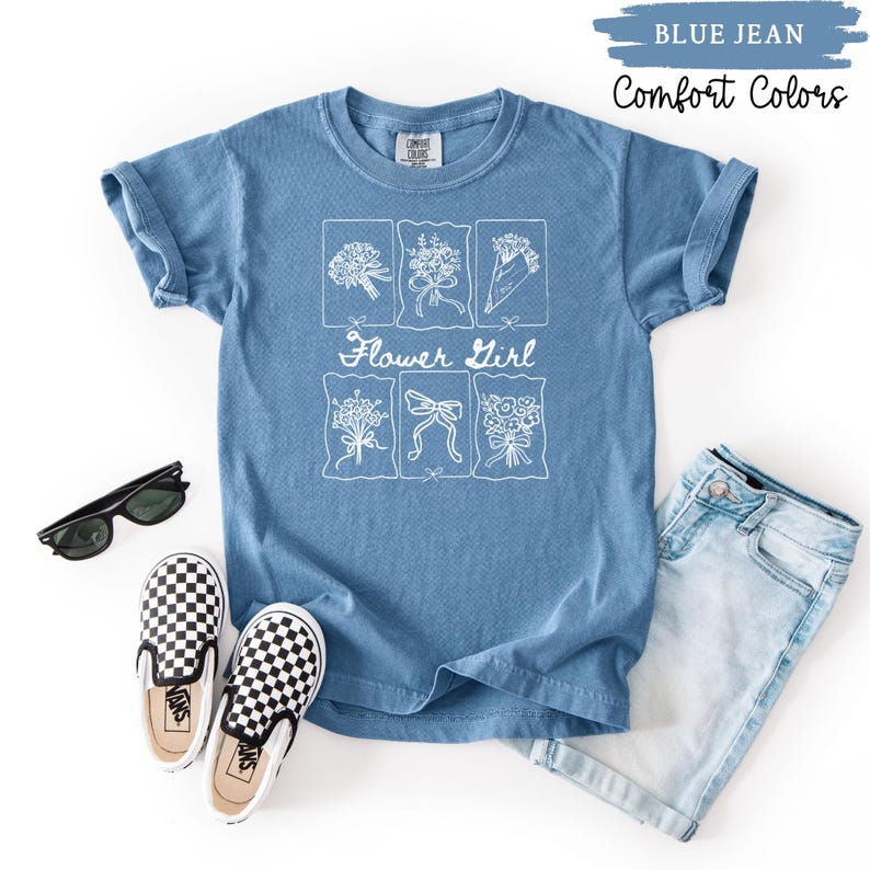 May include: A blue jean Comfort Colors t-shirt with a white floral design and the words "Flower Girl". The shirt is styled with sunglasses, checkered slip-on shoes, and denim shorts.