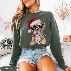 May include: Green sweatshirt featuring a Boxer dog wearing a Santa hat and sunglasses, blowing a bubblegum bubble. The dog is adorned with Christmas lights. The word "HEMP" is at the bottom of the image.