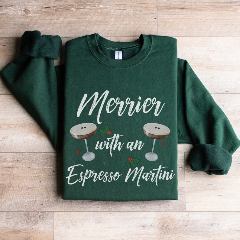 May include: A green sweatshirt with the text "Merrier with an Espresso Martini" and two illustrations of espresso martinis with holly and berries.