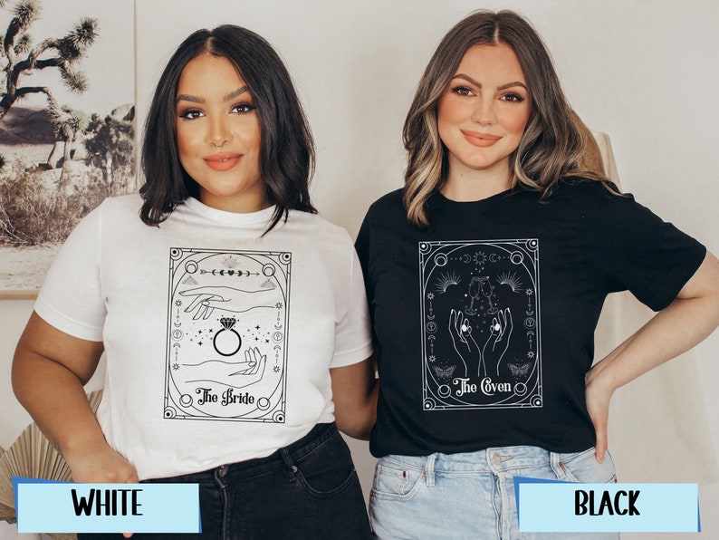 May include: Two women wearing t-shirts with a black and white graphic design. The graphic features a hand holding a ring with the text "The Bride" on one shirt and a hand holding a crystal with the text "The Coven" on the other shirt. The shirts are available in white and black.