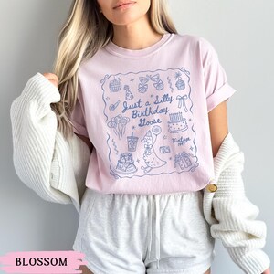 May include: A light pink t-shirt with a blue illustration featuring a goose, cake, and balloons. The text "Just a Silly Birthday Goose" is above the goose. The word "Vintage" and the year "1993" are also included.