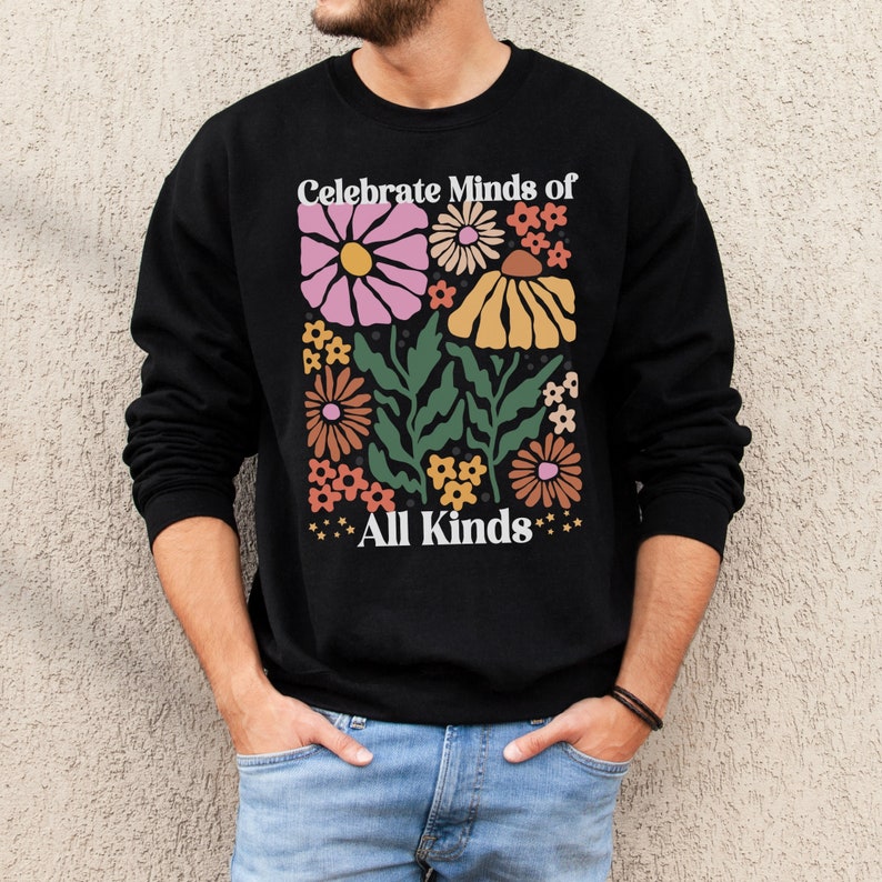 May include: Black sweatshirt with a floral design in pink, yellow, orange, and green. The text "Celebrate Minds of All Kinds" is printed above and below the flowers in white. The sweatshirt is a crew neck style.
