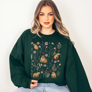 May include: A dark green sweatshirt with a graphic print of capybaras and flowers. The capybaras are brown and the flowers are pink, purple, and red.