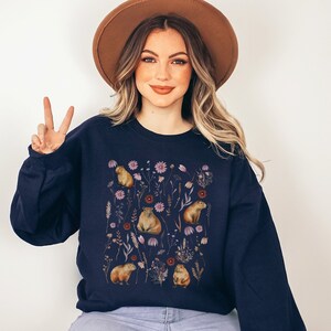 May include: A navy blue sweatshirt with a graphic print of capybaras and flowers. The capybaras are brown and the flowers are pink, purple, and white.