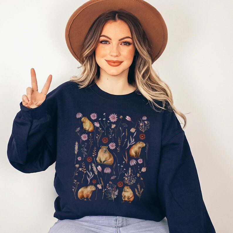 May include: A navy blue sweatshirt with a graphic print of capybaras and flowers. The capybaras are brown and the flowers are pink, purple, and white.