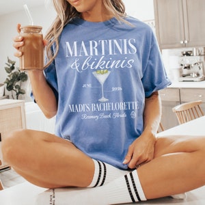 May include: Blue t-shirt with white text that reads "MARTINIS & bikinis" with a martini glass graphic and the text "JUNE 2026 MADI'S BACHELORETTE Rosemary Beach, Florida"