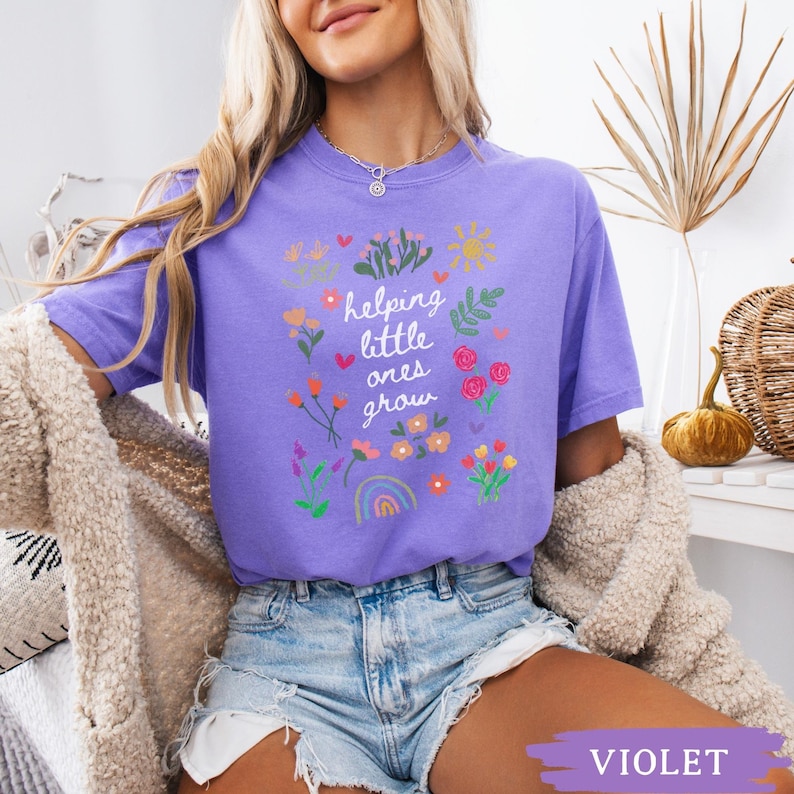 May include: A purple t-shirt with a floral design and the text "helping little ones grow".