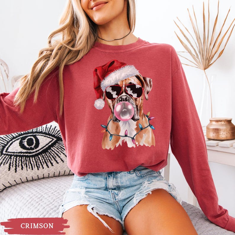 May include: Crimson-colored sweatshirt featuring a Boxer dog wearing sunglasses and a Santa hat, blowing a bubblegum bubble. The dog is adorned with Christmas lights. The word "CRIMSON" is at the bottom of the image.
