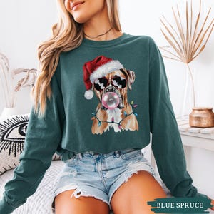 May include: A teal long-sleeve sweatshirt featuring a Boxer dog wearing sunglasses and a Santa hat, blowing a bubblegum bubble. The dog is adorned with Christmas lights. The text "BLUE SPRUCE" is at the bottom.